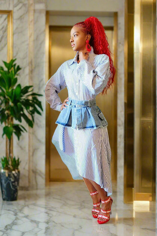 Woman in a stylish outfit with a blue and white striped shirt and skirt, standing against a beige wall.